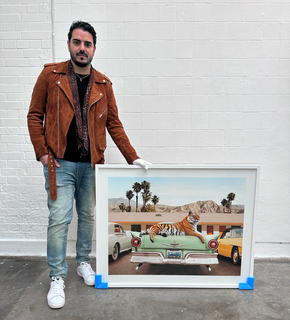 Paul Fuentes holding a framed artwork  TIGER MOTEL, of a  a tiger on a classic car with palm trees in the background. at The Other Art Fair