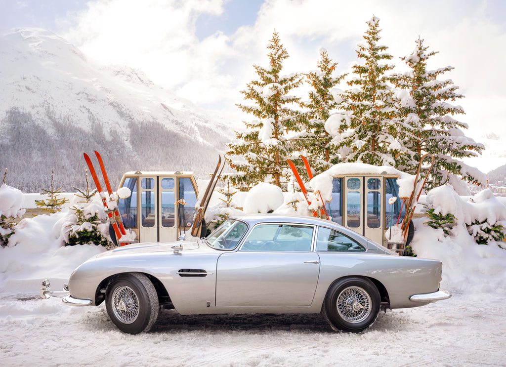 A fine art print featuring a classic Aston Martin DB5 parked in a snowy alpine setting with ski equipment photographed by Paul Fuentes