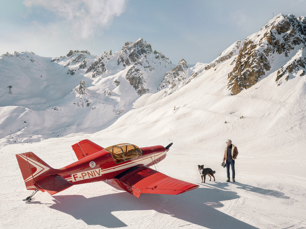 Photography by Paul Fuentes depicting a red airplane on a snowy mountain background with a person standing beside it.