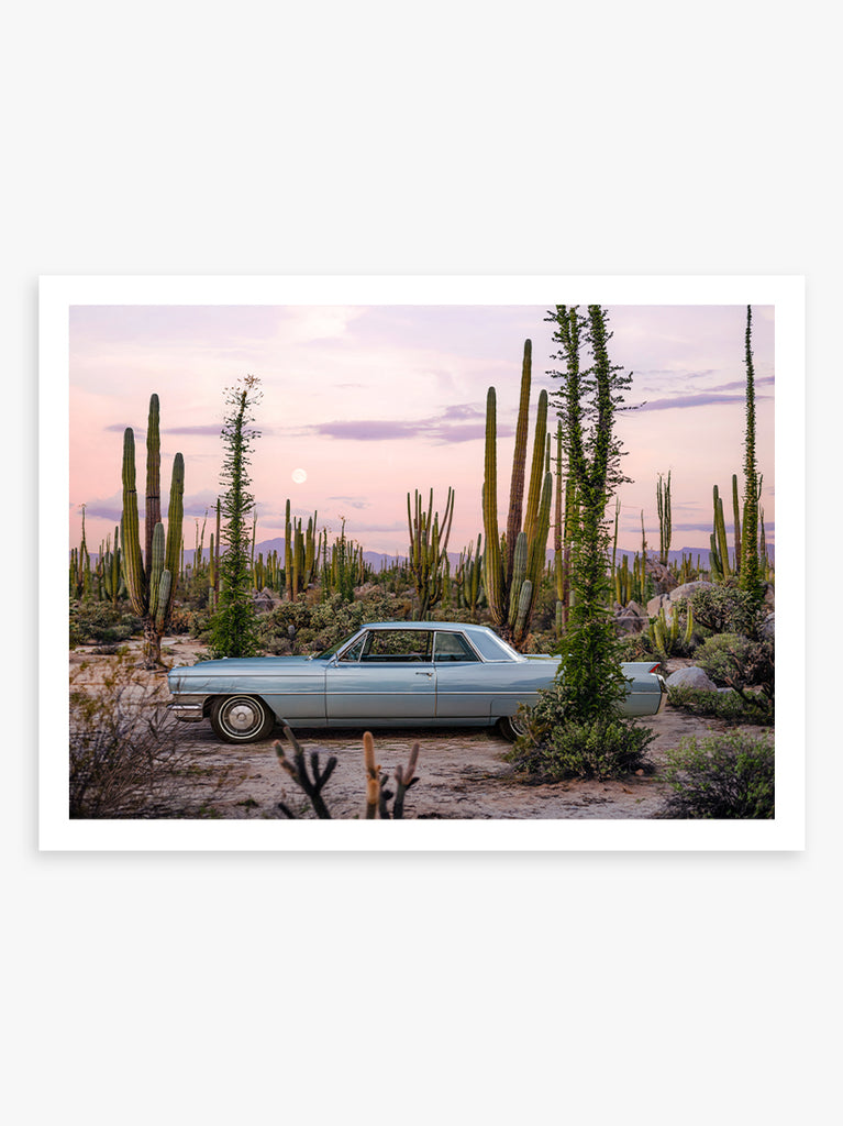 A photograph of a 1964 Cadillac Coupe DeVille in Valle de los Cirios, Baja California desert, Mexico, with a colorful sunset sky in the background. fine art photography by Paul Fuentes.