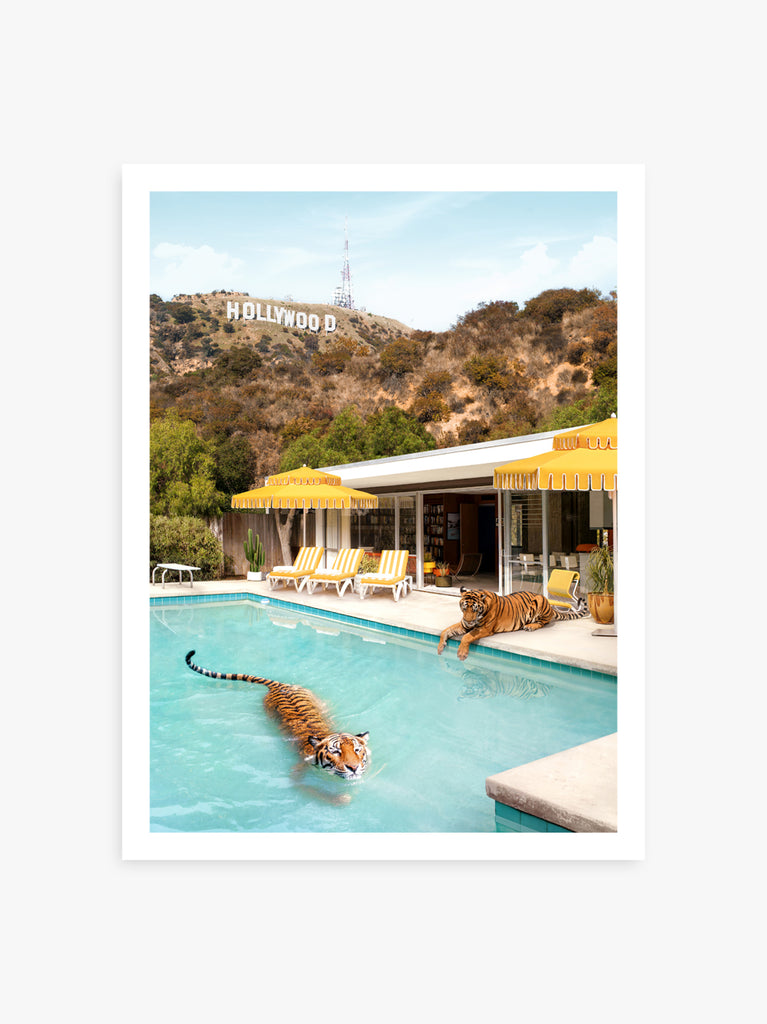 A vintage style photograph featuring two tigers lounging by a poolside with 'Hollywood' sign in the background and yellow 'Double Decker' umbrellas. fine art photograph by Paul Fuentes.