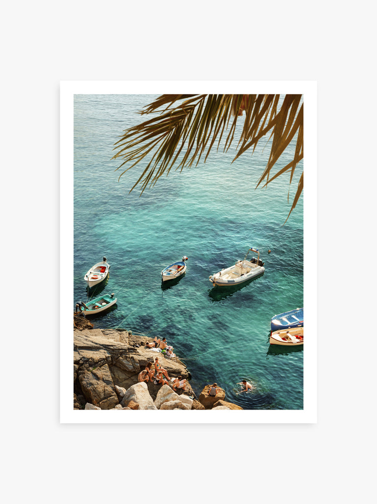 print of Boats anchored near rocky shores with palm leaves in the foreground, fine art photograph by Paul Fuentes.