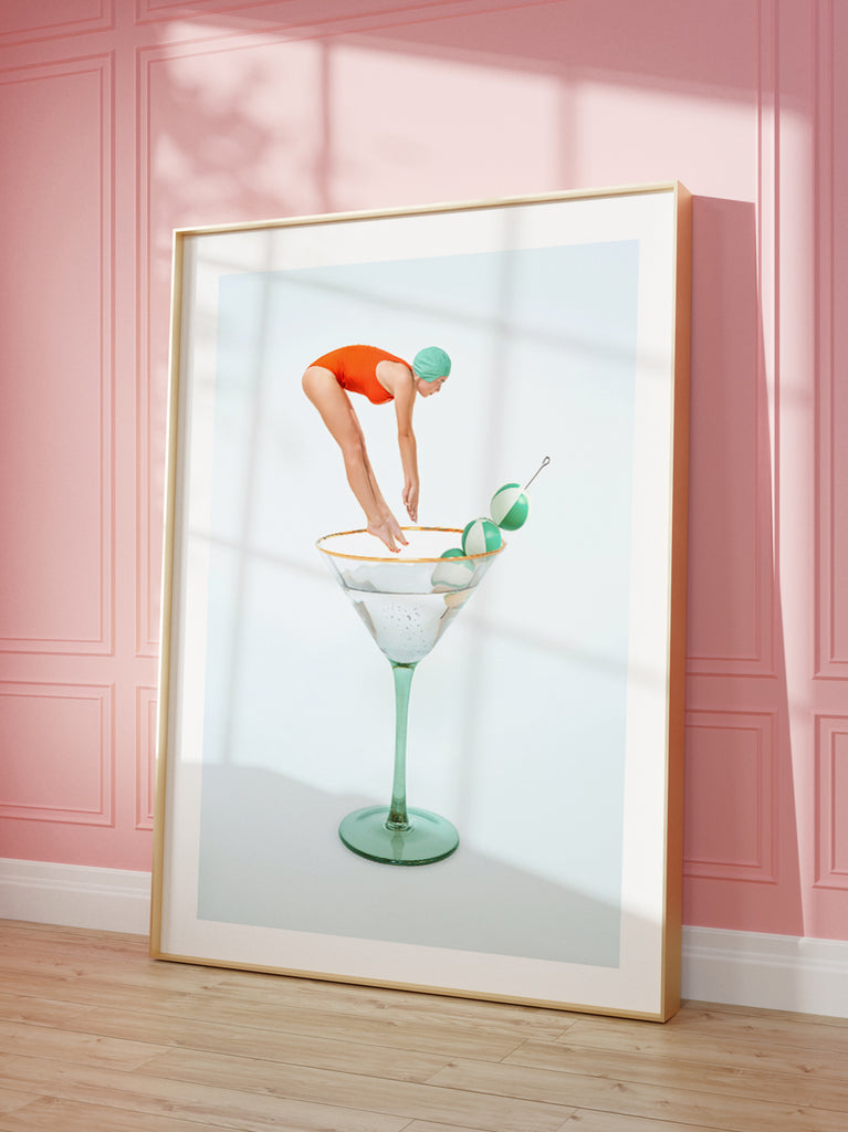 Martini framed artwork by Paul Fuentes with a woman in a red swimsuit diving into a martini glass, with a beach ball olive garnish on the side.