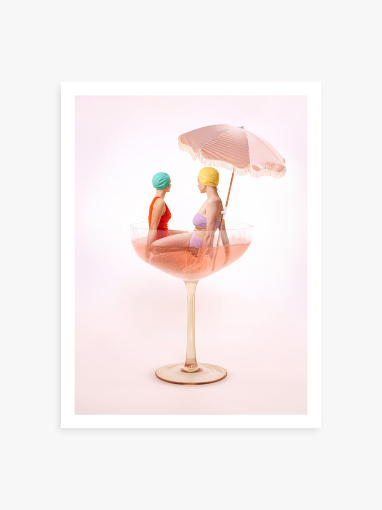 artistic fine art print by Paul Fuentesnfeaturing two women sitting in a champagne glass with a pink umbrella, against a pink background.
