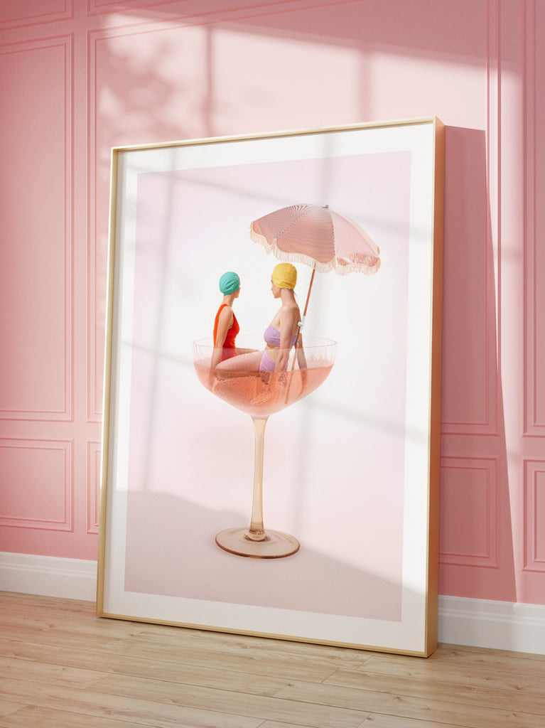 artistic fine art print by Paul Fuentesnfeaturing two women sitting in a champagne glass with a pink umbrella, against a pink background.