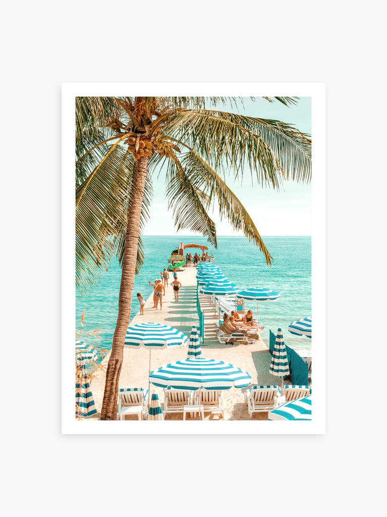 A vibrant print featuring a beach scene in Antibes with palm trees, beach umbrellas, and a boardwalk leading to the ocean. fine art photography by Paul Fuentes.