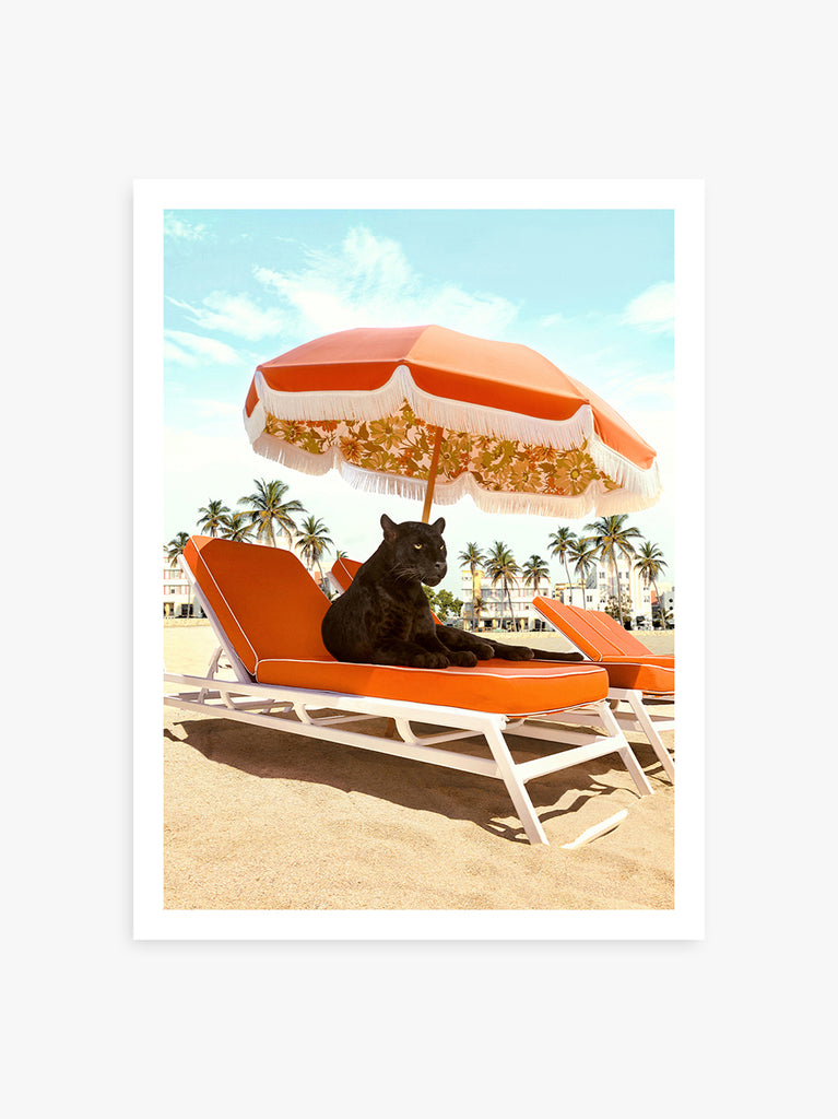 retro beach vibe with a black panther lounging on an orange beach chair under a vintage  umbrella with palm trees in the background. fine art print by Paul Fuentes.