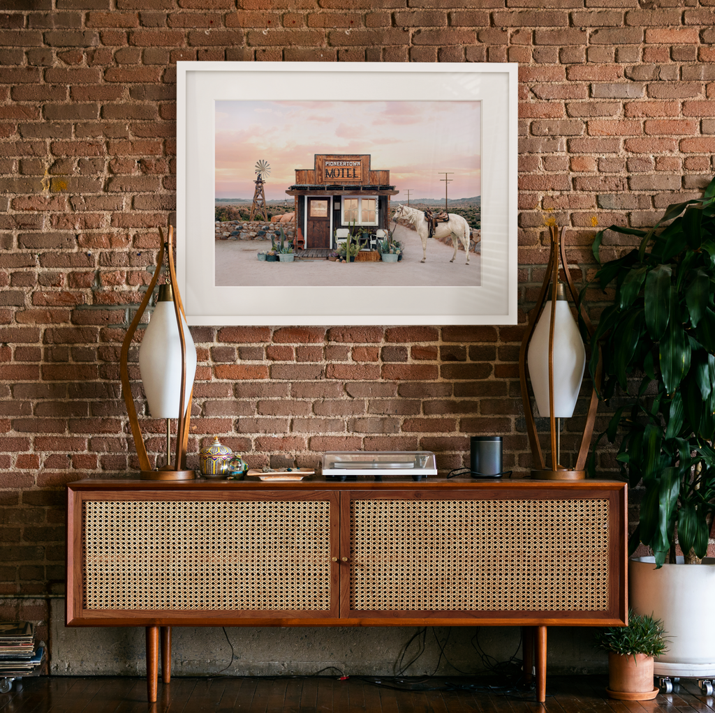 framed artwork of pioneer town motel, photograph by Paul Fuentes showcasing a desert landscape with a horse and cacti in the foreground.