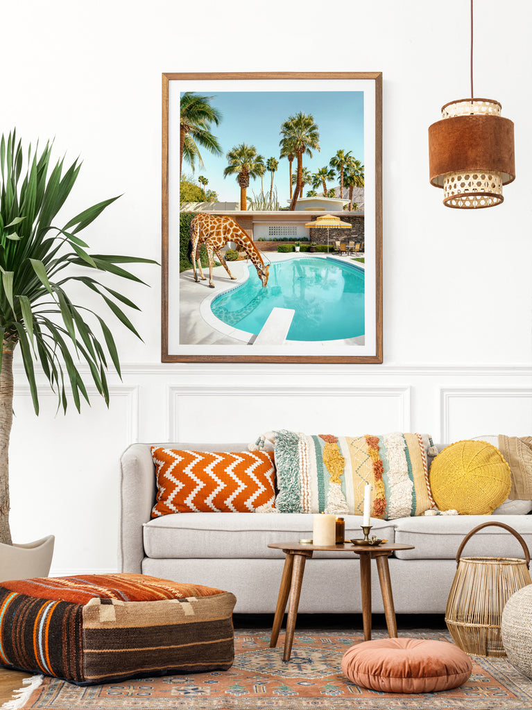 Framed artwork of a giraffe drinking from a pool with palm trees and a palm springs house in the background, representing mid-century poolside glamour fine art photography by Paul Fuentes.