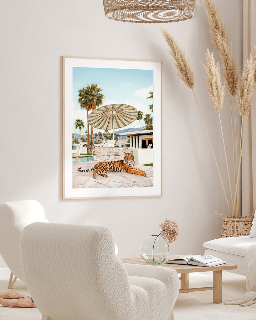 Framed artwork featuring a tiger lying down a umbrella and palm trees in the background, representing a playful and vintage Palm Springs vibe, fine art photography by Paul Fuentes